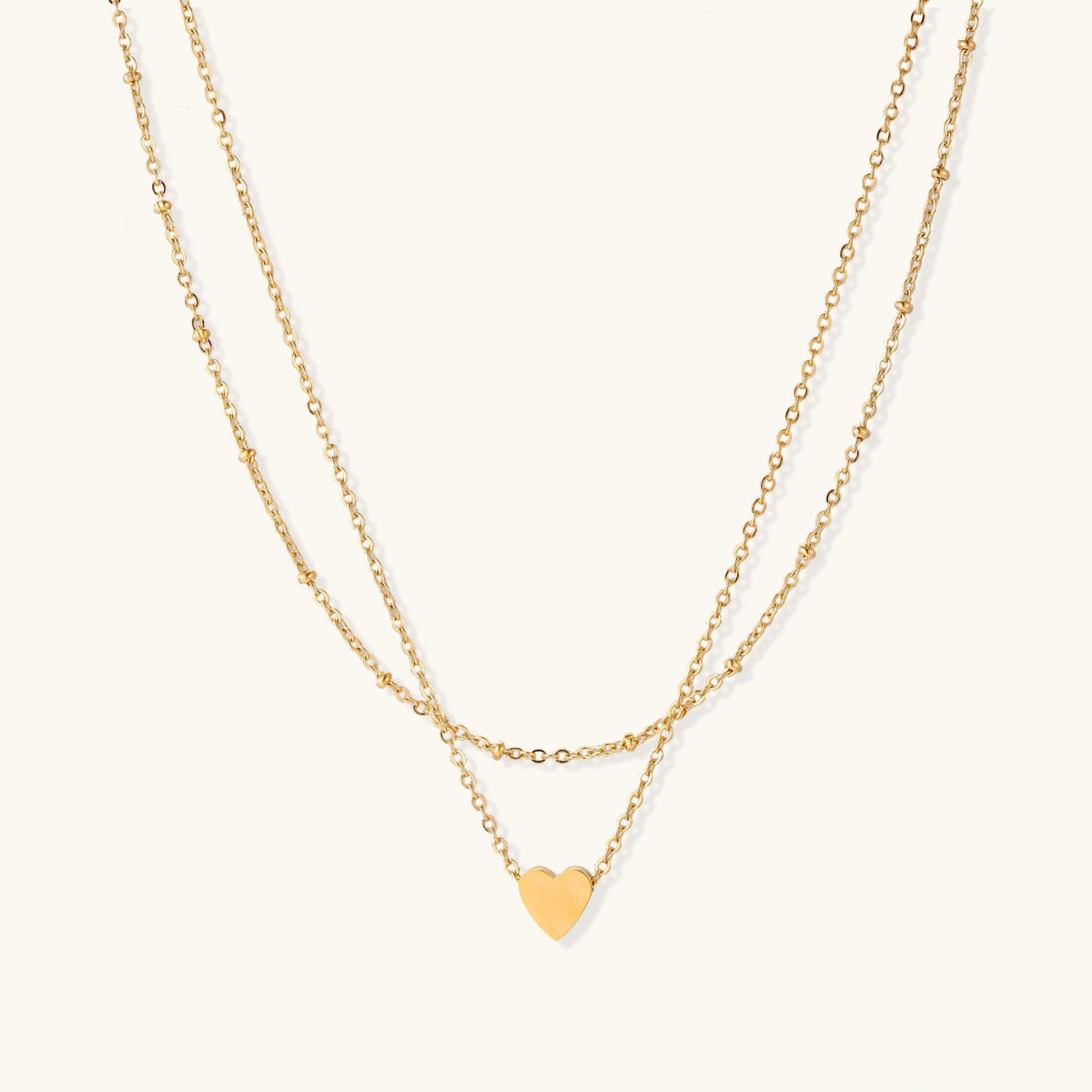 Delicate double-chain gold necklace with tiny heart pendant on cream background
