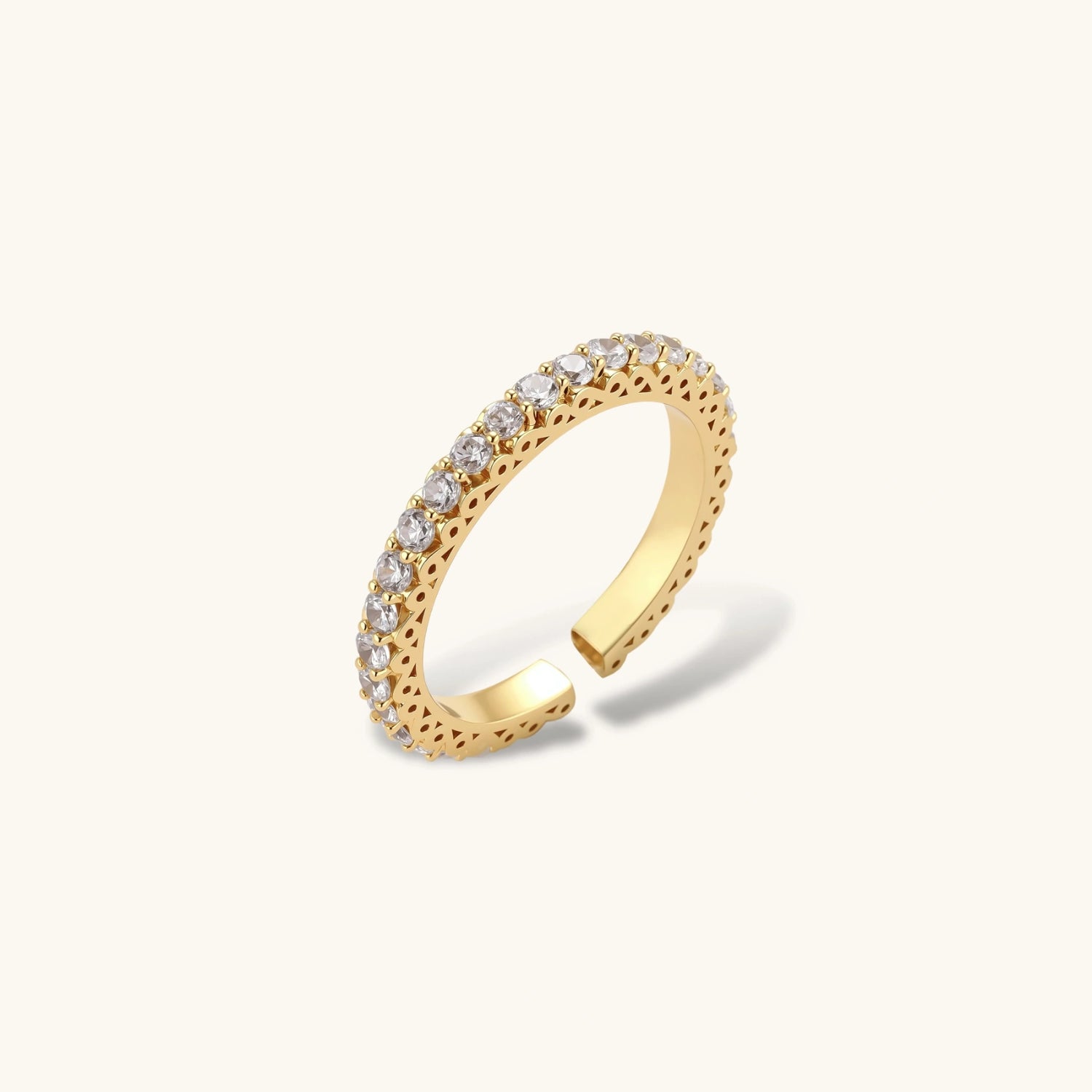 Close-up of adjustable gold-plated ring with continuous row of round zirconia stones on neutral background.