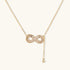 Gold infinity pendant with baguette crystals on adjustable chain against cream background.