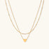 Delicate double-chain gold necklace with tiny heart pendant on cream background