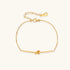 Delicate gold chain bracelet with minimalist bar and centered knot detail on cream background